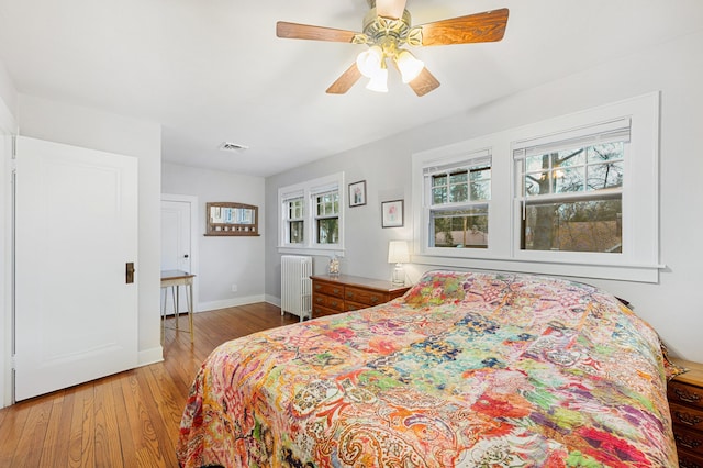 bedroom with radiator heating unit, visible vents, light wood-type flooring, baseboards, and ceiling fan