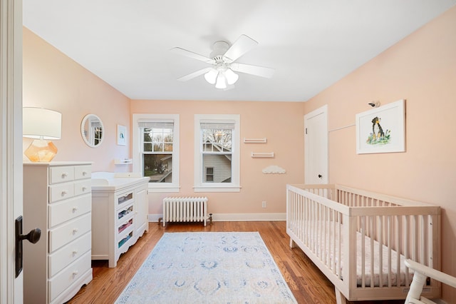 bedroom featuring radiator heating unit, a crib, baseboards, and light wood-style flooring