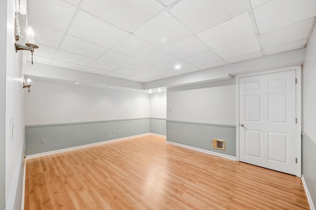 finished below grade area featuring wood finished floors, a wainscoted wall, and a paneled ceiling