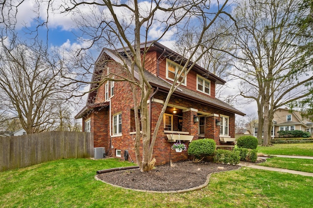 view of front facade featuring brick siding, fence, central AC, and a front yard
