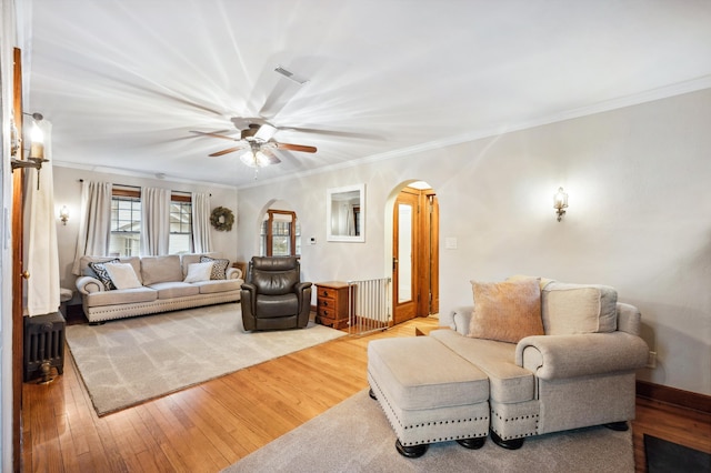 living area with a ceiling fan, wood finished floors, arched walkways, and crown molding