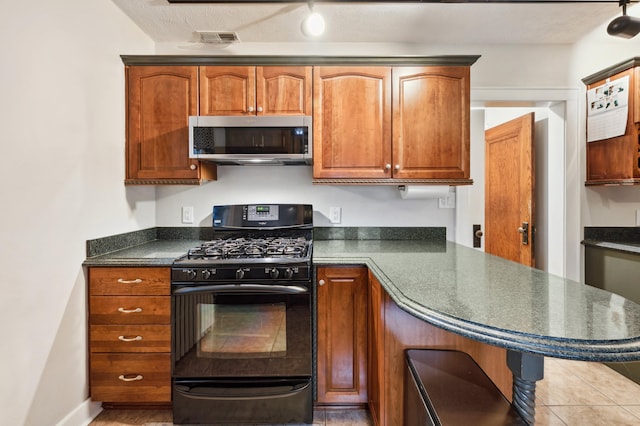 kitchen with dark countertops, brown cabinetry, stainless steel microwave, gas stove, and visible vents