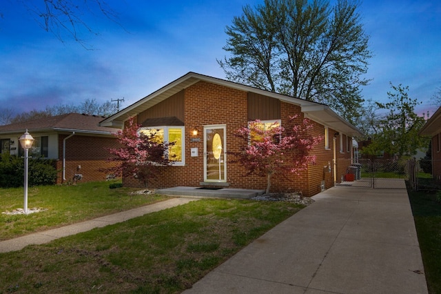 view of front of home featuring brick siding, fence, a yard, and concrete driveway