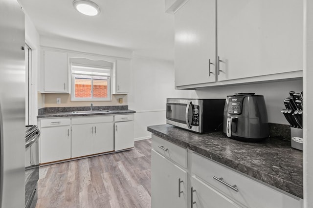 kitchen with stainless steel appliances, white cabinetry, a sink, and light wood-style floors