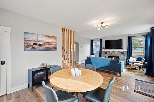 dining room featuring light wood finished floors, a fireplace, baseboards, and arched walkways