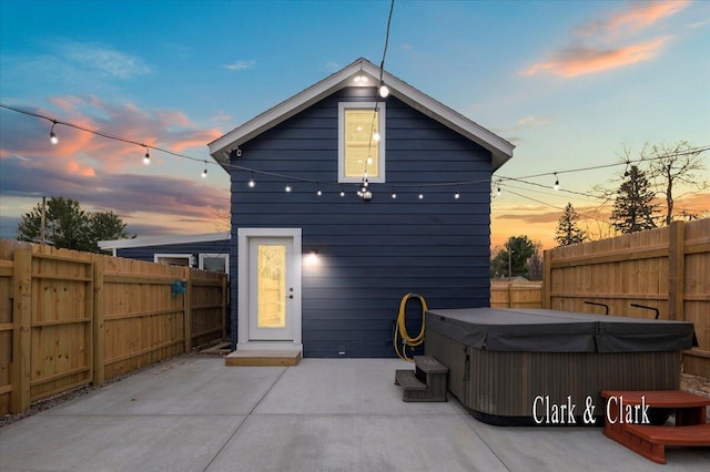 back of house at dusk featuring a fenced backyard, a hot tub, and a patio