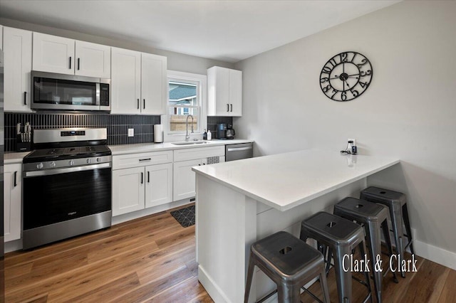 kitchen with white cabinets, a sink, backsplash, a kitchen bar, and appliances with stainless steel finishes