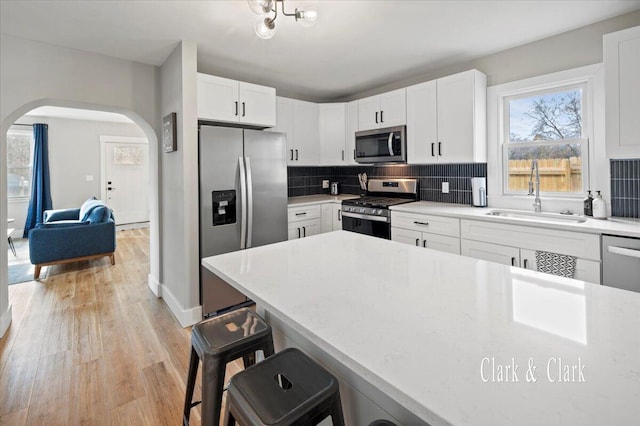 kitchen with light wood-style flooring, arched walkways, a sink, tasteful backsplash, and appliances with stainless steel finishes