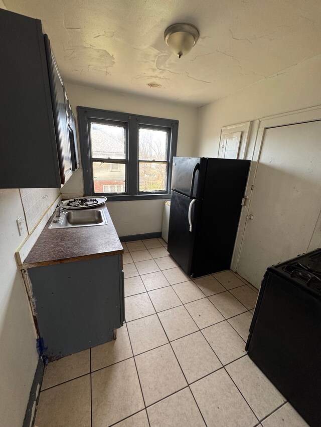 kitchen with a sink, baseboards, black appliances, dark cabinets, and light tile patterned floors