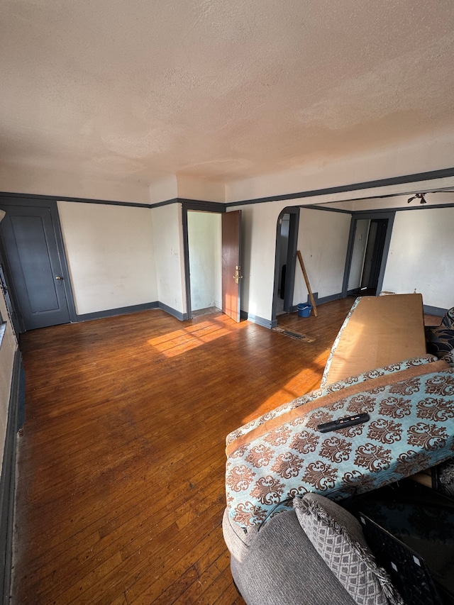 empty room with baseboards, arched walkways, a textured ceiling, and hardwood / wood-style floors