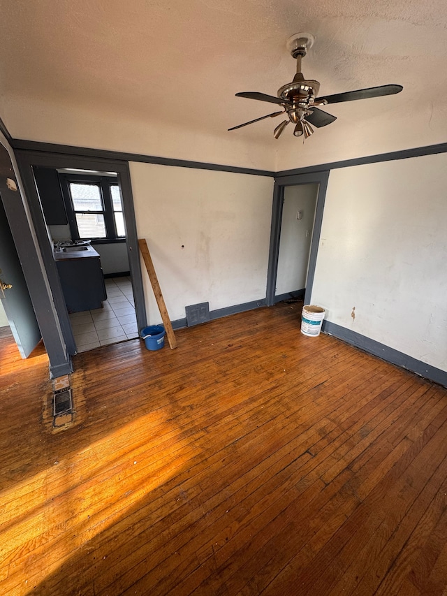 empty room featuring hardwood / wood-style flooring, ceiling fan, baseboards, and visible vents