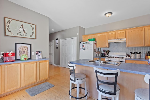 kitchen featuring light brown cabinets, a kitchen breakfast bar, white appliances, light wood-style flooring, and under cabinet range hood