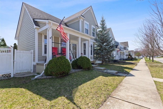 view of front facade featuring a front lawn, a shingled roof, covered porch, fence, and a residential view
