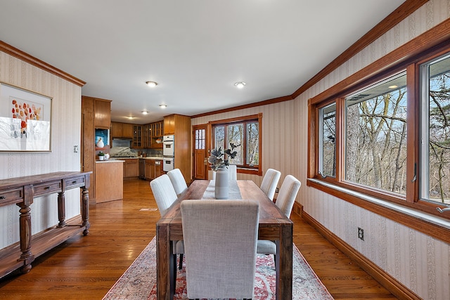 dining space featuring wallpapered walls, baseboards, dark wood-type flooring, and ornamental molding