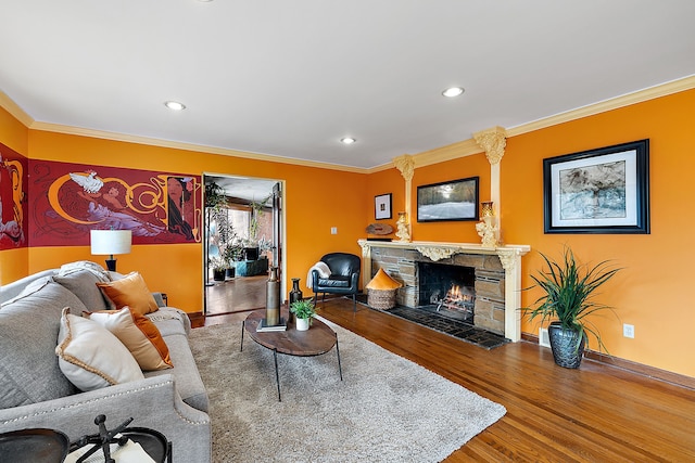 living area with wood finished floors, a stone fireplace, and ornamental molding