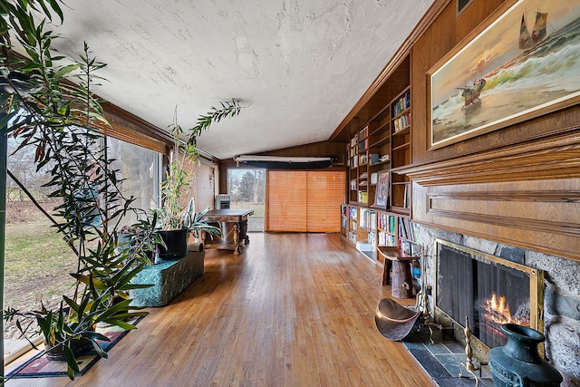 living area with hardwood / wood-style floors, wood walls, vaulted ceiling, a fireplace, and built in features
