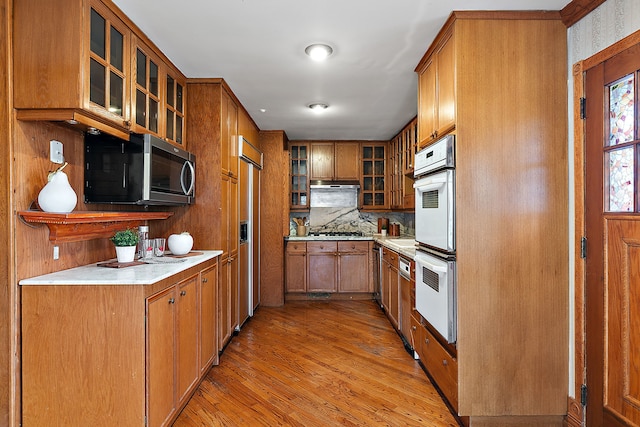 kitchen featuring brown cabinetry, appliances with stainless steel finishes, and glass insert cabinets