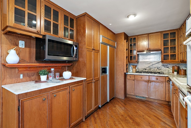 kitchen with brown cabinetry, under cabinet range hood, and stainless steel appliances