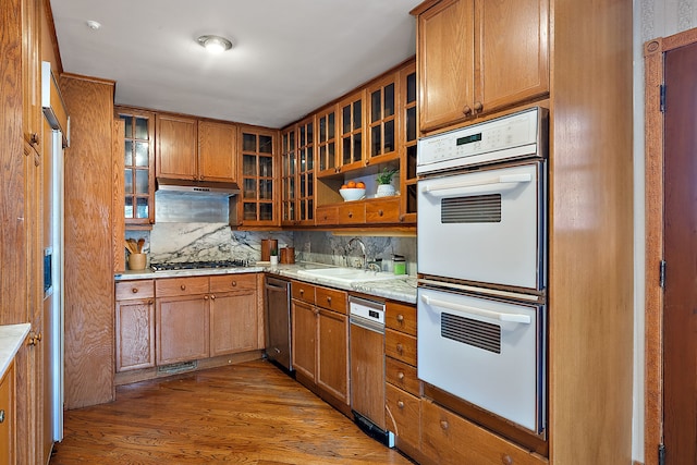 kitchen with under cabinet range hood, white double oven, a sink, decorative backsplash, and brown cabinetry