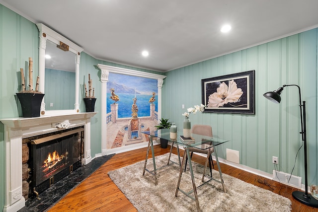 office area featuring a fireplace with flush hearth, baseboards, crown molding, and wood finished floors