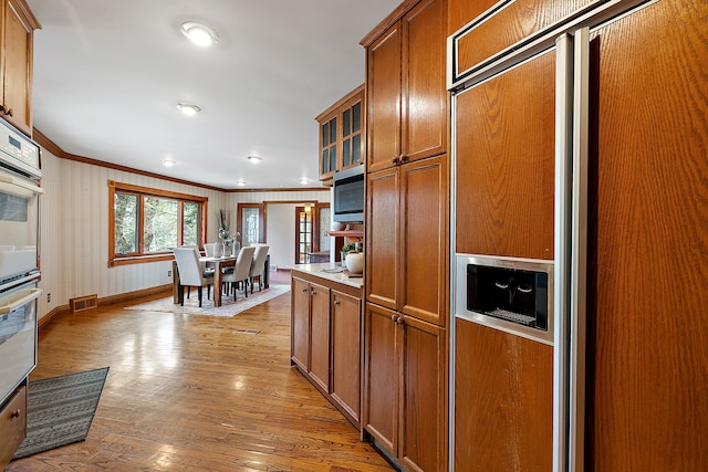 kitchen with stainless steel microwave, brown cabinetry, visible vents, and ornamental molding