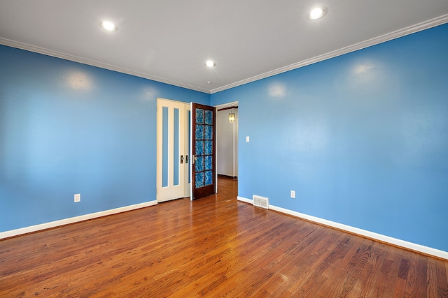 empty room featuring baseboards, crown molding, wood finished floors, and visible vents