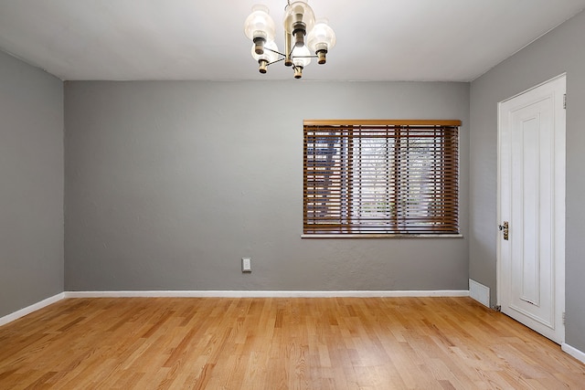 empty room with a chandelier, wood finished floors, visible vents, and baseboards