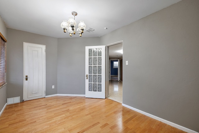 empty room with baseboards, a notable chandelier, light wood-style floors, and visible vents