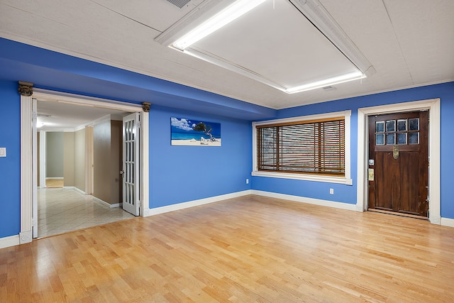 empty room featuring attic access, baseboards, wood finished floors, and crown molding