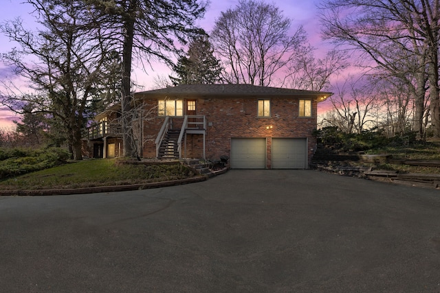 view of front of house with brick siding, an attached garage, stairway, and aphalt driveway