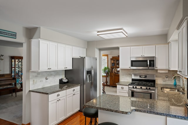 kitchen featuring decorative backsplash, appliances with stainless steel finishes, a sink, a peninsula, and dark stone countertops