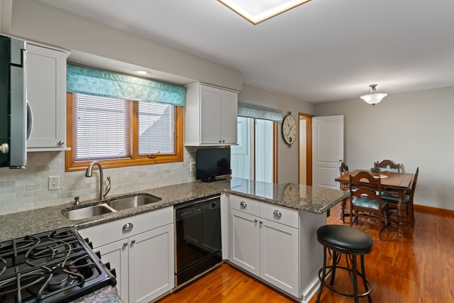kitchen featuring range with gas stovetop, a peninsula, black dishwasher, a sink, and light wood-style flooring