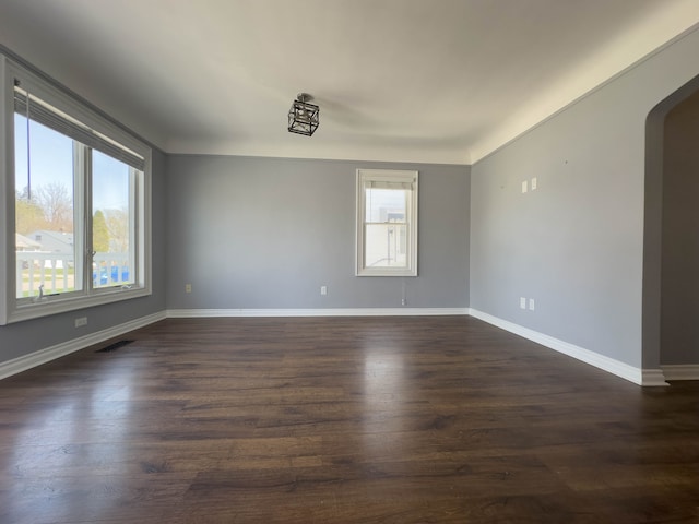 spare room with healthy amount of natural light, arched walkways, and dark wood-type flooring
