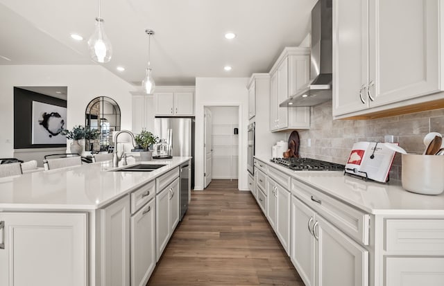 kitchen featuring stainless steel appliances, a sink, wood finished floors, wall chimney range hood, and light countertops