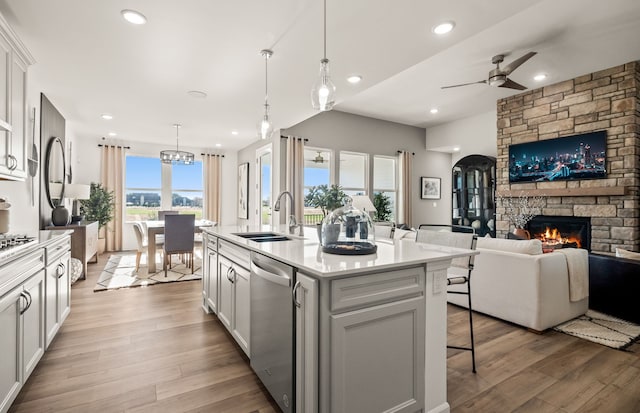 kitchen with stainless steel dishwasher, open floor plan, ceiling fan with notable chandelier, a stone fireplace, and a breakfast bar area