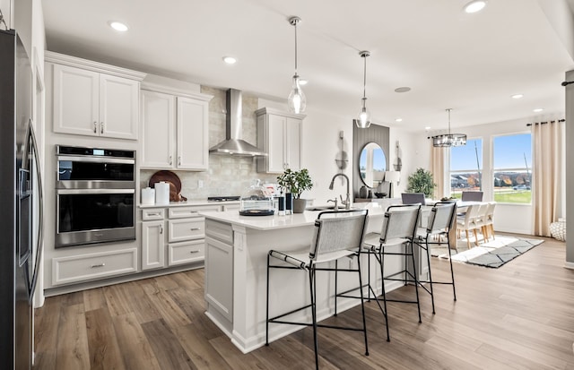 kitchen with wall chimney exhaust hood, stainless steel appliances, light wood finished floors, backsplash, and light countertops