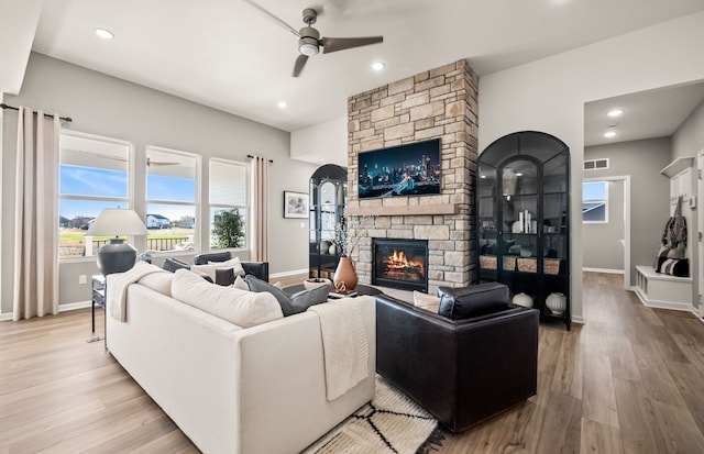 living room with ceiling fan, wood finished floors, a stone fireplace, and visible vents