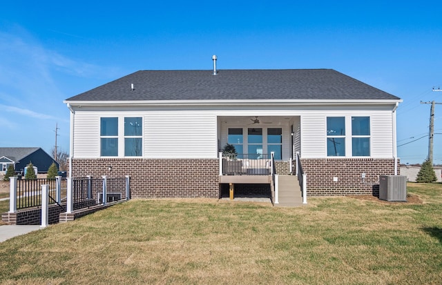 back of house featuring roof with shingles, cooling unit, fence, brick siding, and a lawn