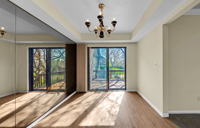 interior space with baseboards, an inviting chandelier, wood finished floors, and a raised ceiling