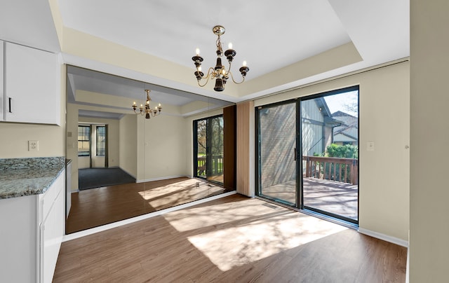 unfurnished dining area featuring a wealth of natural light, an inviting chandelier, wood finished floors, and baseboards