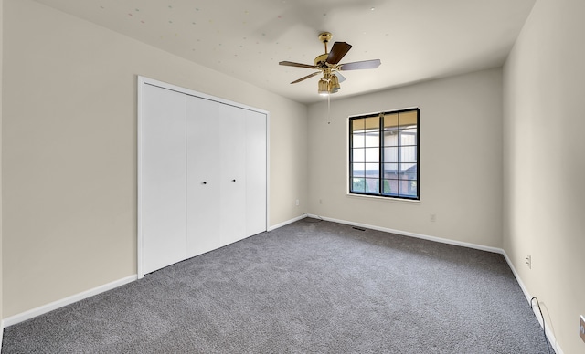 unfurnished bedroom with dark colored carpet, a closet, baseboards, and ceiling fan