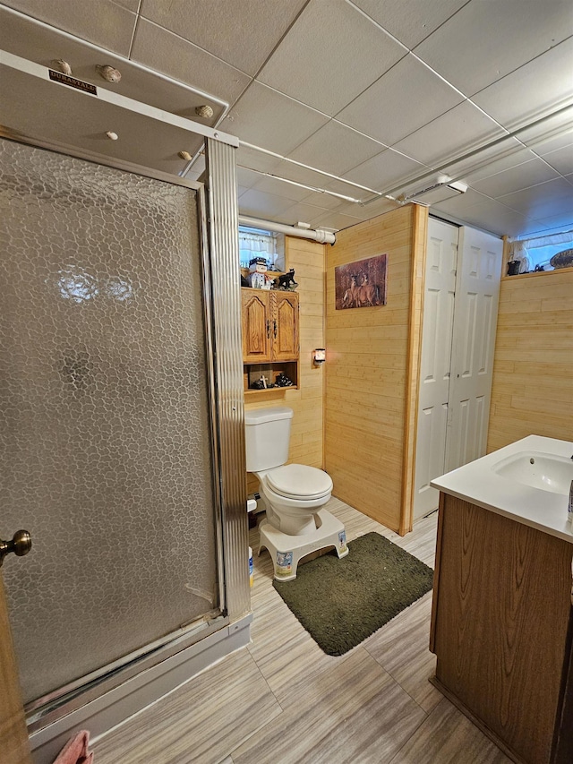 full bathroom featuring a shower stall, wood finished floors, vanity, wooden walls, and toilet