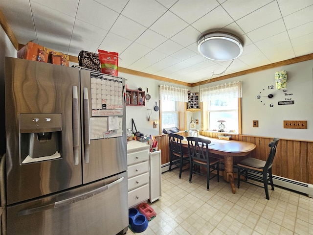 kitchen with a baseboard heating unit, wooden walls, light floors, a wainscoted wall, and stainless steel refrigerator with ice dispenser