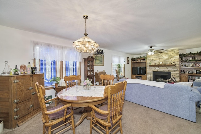 9155 Ivanhoe Dr, Onekama, MI 49675 - dining space featuring light carpet, a stone fireplace, and ceiling fan with notable chandelier