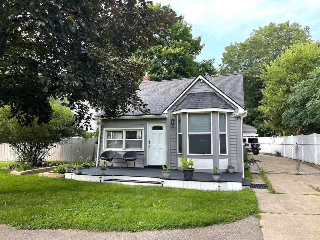 view of front of property with fence, a front lawn, roof with shingles, and a deck