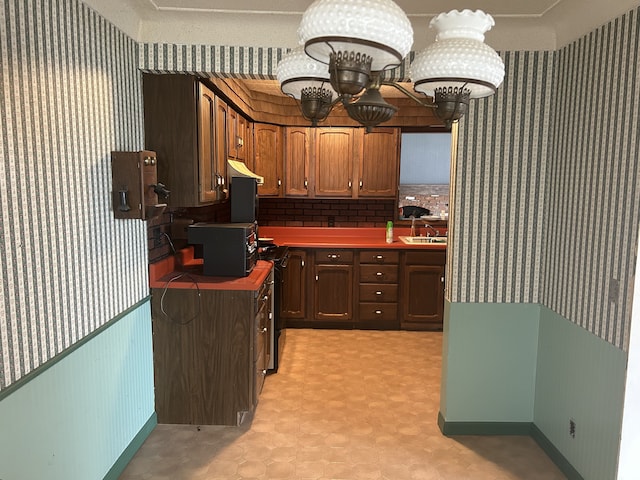 kitchen featuring wallpapered walls, a notable chandelier, under cabinet range hood, and a sink