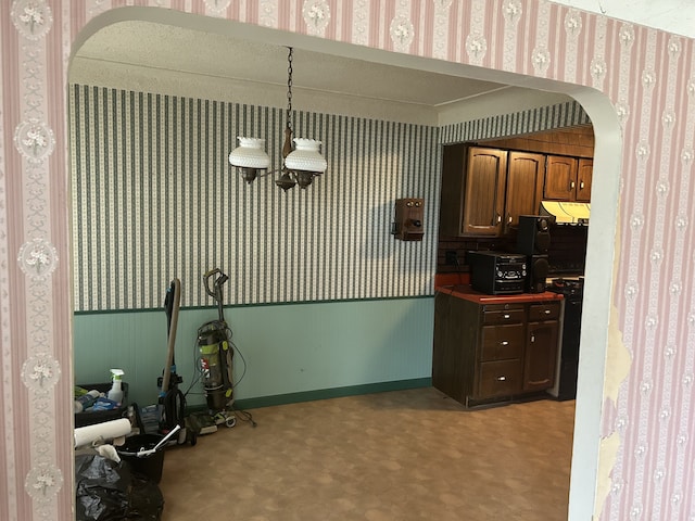 kitchen featuring arched walkways, black gas stove, pendant lighting, and wallpapered walls