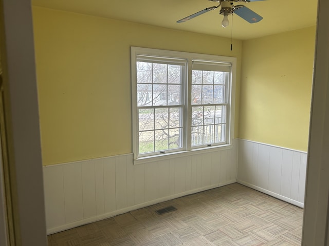 spare room with baseboards, a ceiling fan, a wainscoted wall, and visible vents
