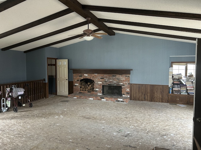 unfurnished living room featuring a fireplace, a wainscoted wall, a ceiling fan, and vaulted ceiling with beams