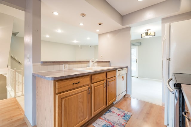 kitchen featuring recessed lighting, brown cabinets, light wood finished floors, a sink, and white appliances